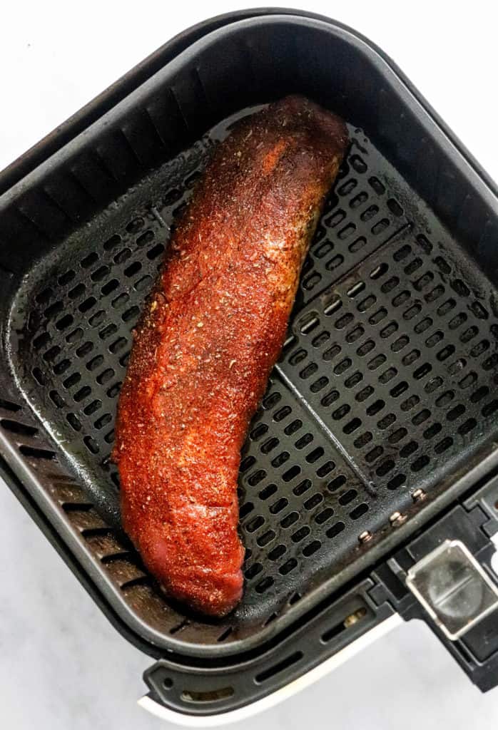 Seasoned raw pork tenderloin in a square black air fryer basket