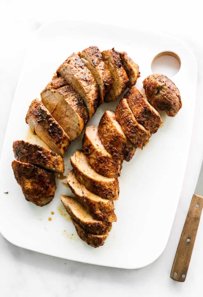 Cooked pork tenderloin sliced on a white cutting board