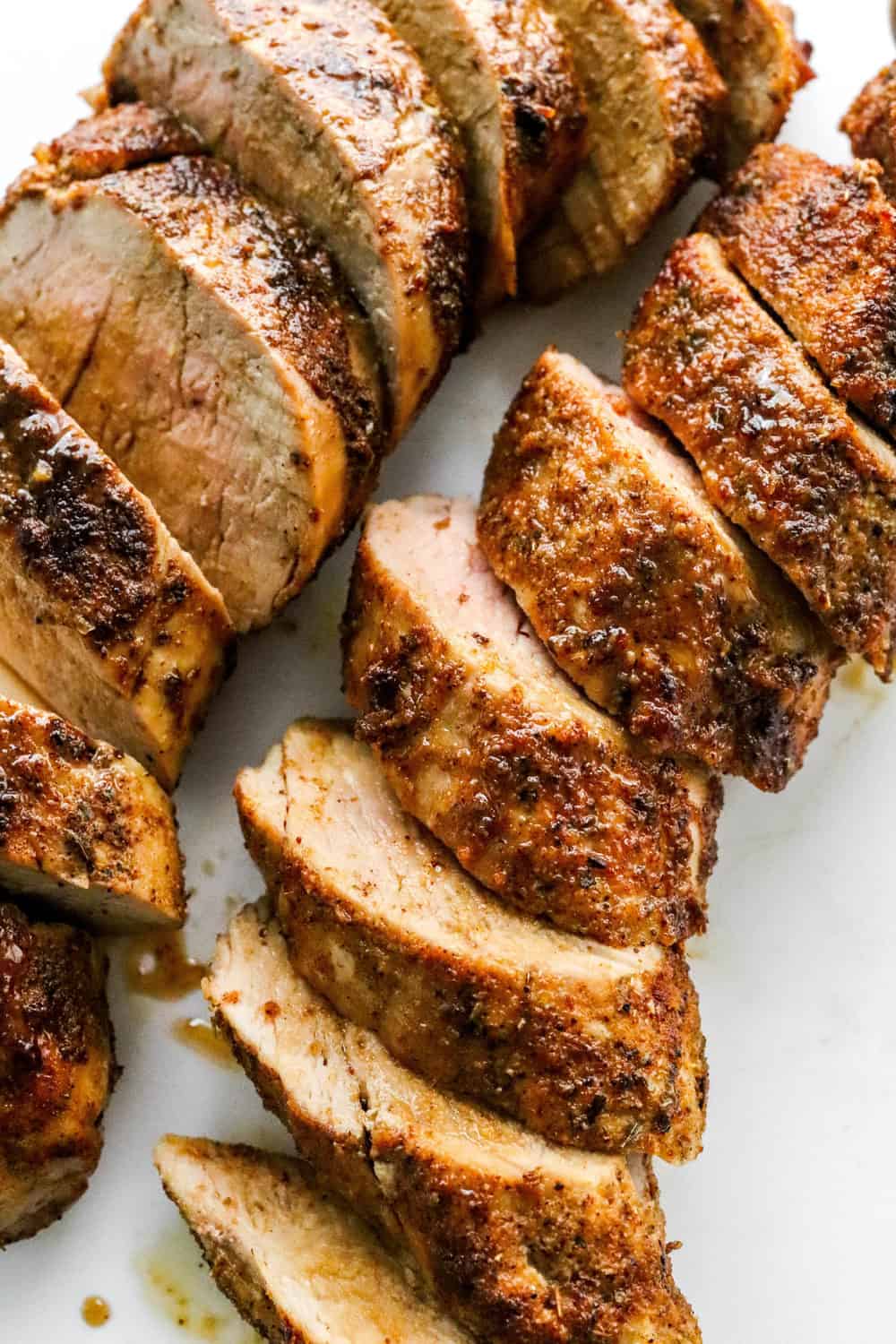 Cooked, seasoned air fryer pork tenderloin sliced on a white cutting board. 