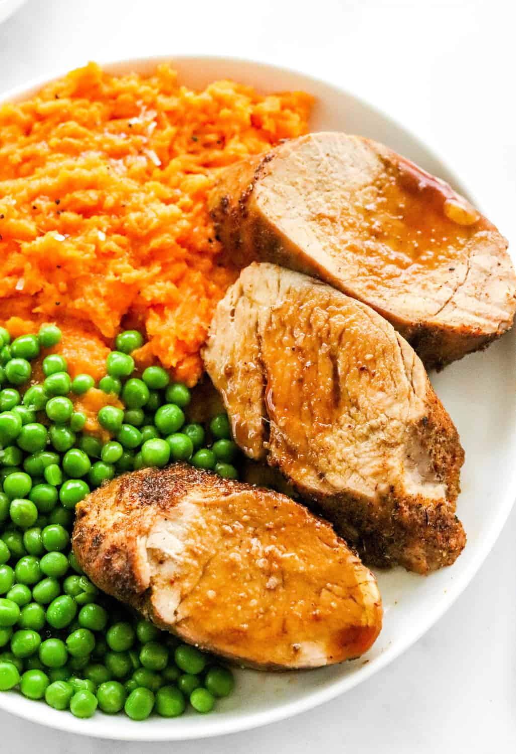 Close up of plate with mashed sweet potato, peas and sliced pork medallions on it. 