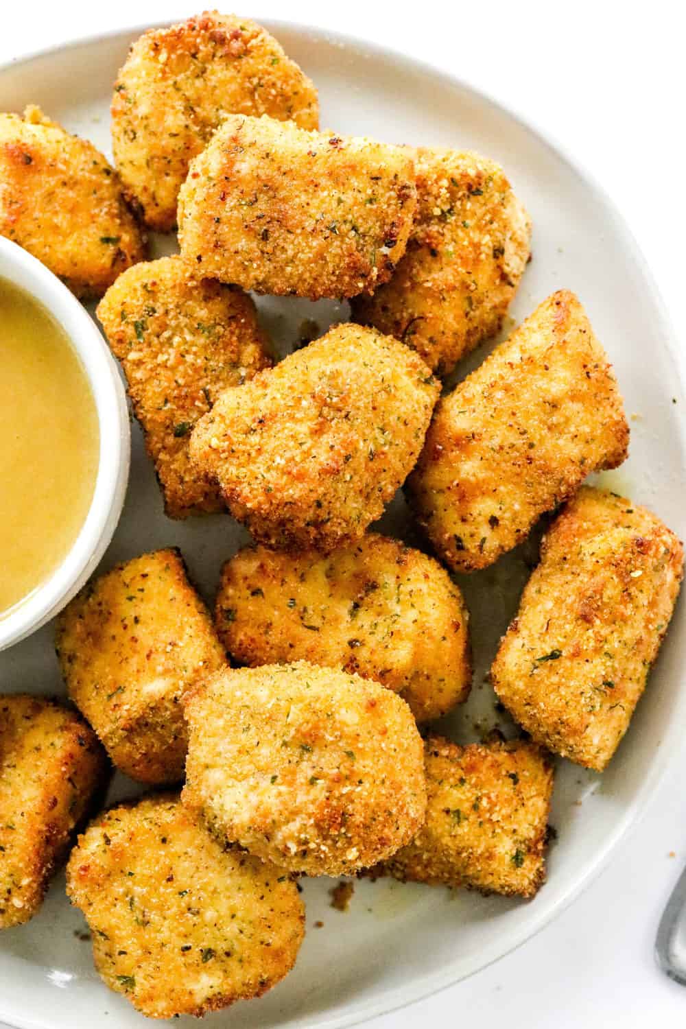 Round plate filled with breaded air fryer chicken nuggets with a mustard dipping sauce in a white dish next to them. 