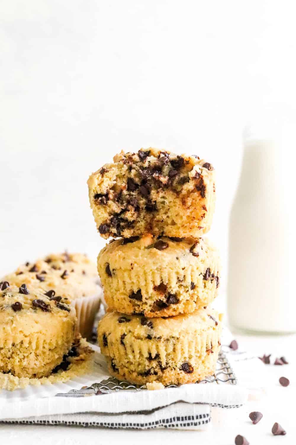 3 chocolate chip muffins stacked on top of one another with a bite taken out of the top on and more muffins next to it. 