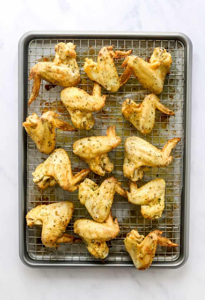 Golden cooked lemon pepper chicken wings on a baking rack on a baking sheet.