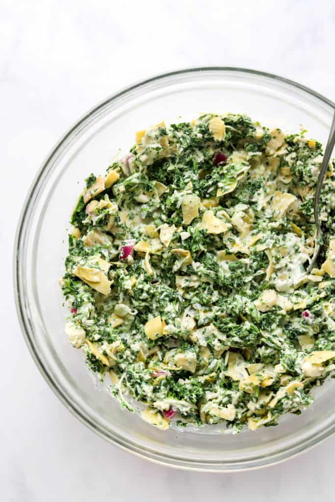Spinach, cheese and artichokes mixed up in a round, glass mixing bowl