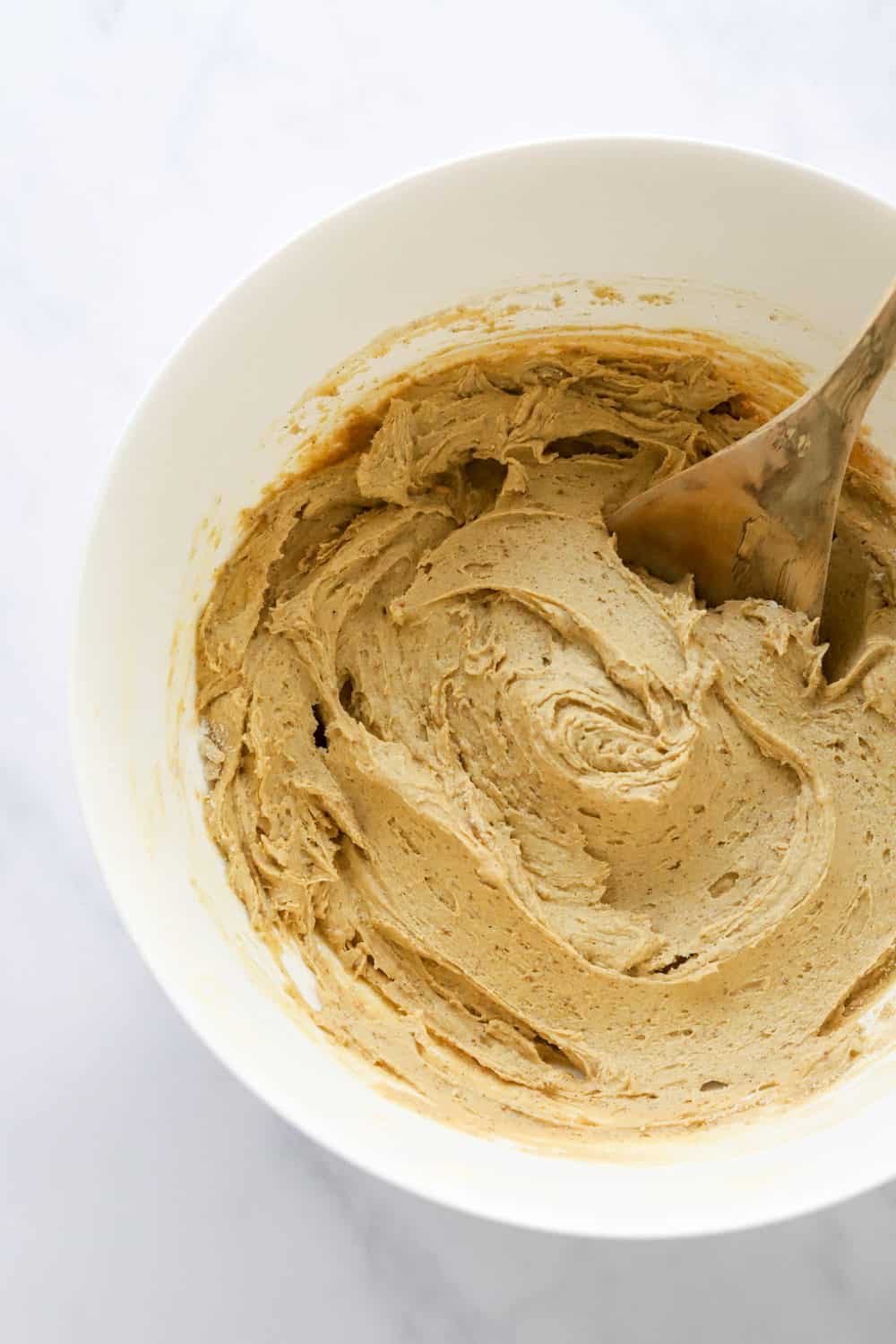 Brown cookie batter in a white mixing bowl with a wooden spoon in it.