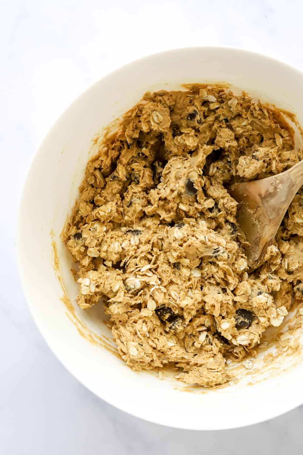 Healthy oatmeal chocolate chip cookie batter mixed up in a mixing bowl with a wooden spoon in the bowl. 