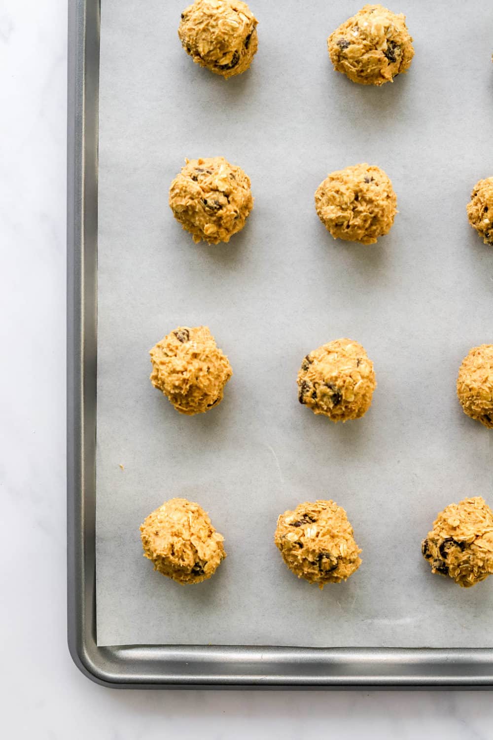 Raw cookie dough rolled in balls spread out on a cookie sheet lined with white parchment paper. 