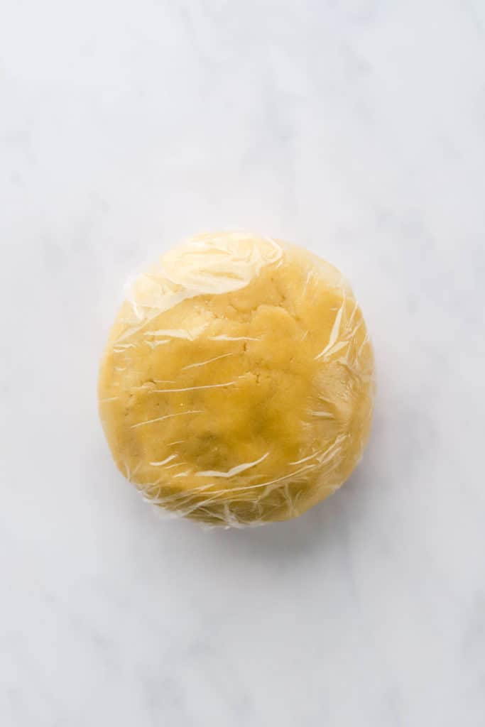 Light brown sugar cookie dough rolled in a ball and wrapped in clear plastic wrap