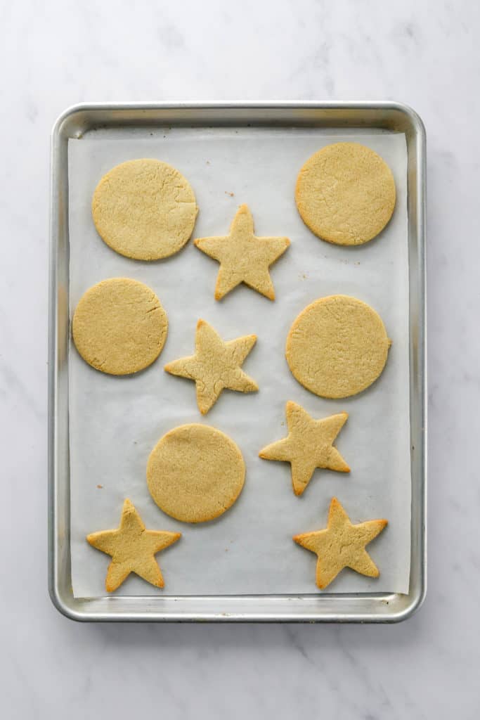 Baked sugar cookies in star and circle shapes on a parchment paper lined baking sheet