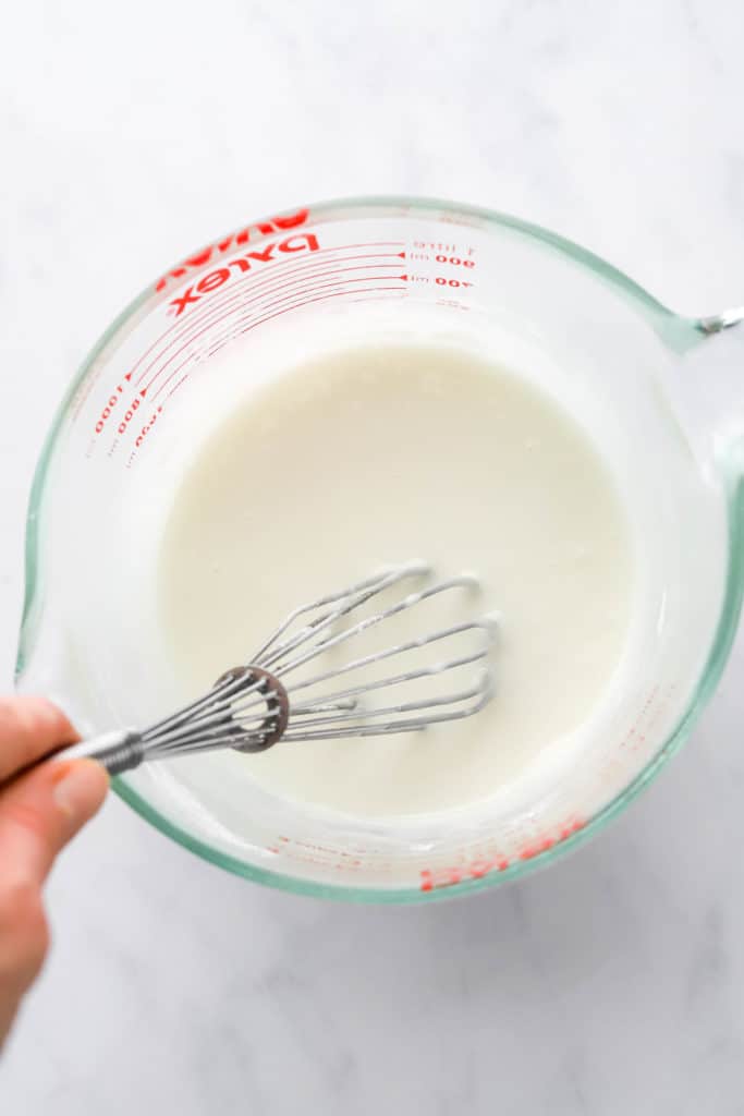 Hand mixing white icing with a metal whisk in  mixing bowl
