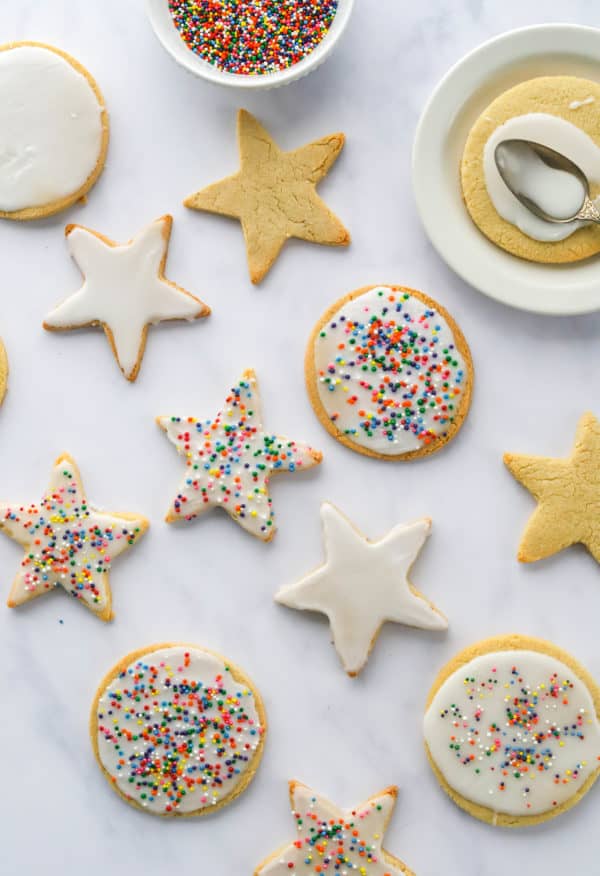 Sugar cookies in circle and star shapes iced with white icing with rainbow sprinkles spread out in a diagonal line