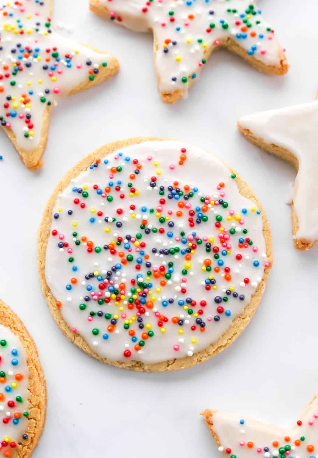 Round gluten free cookies bread with white frosting and sprinkles on top with more iced cookies around it. 