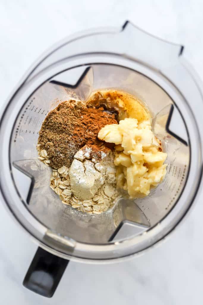 Mashed banana, spices and maple syrup in a clear blender before being blended up. 