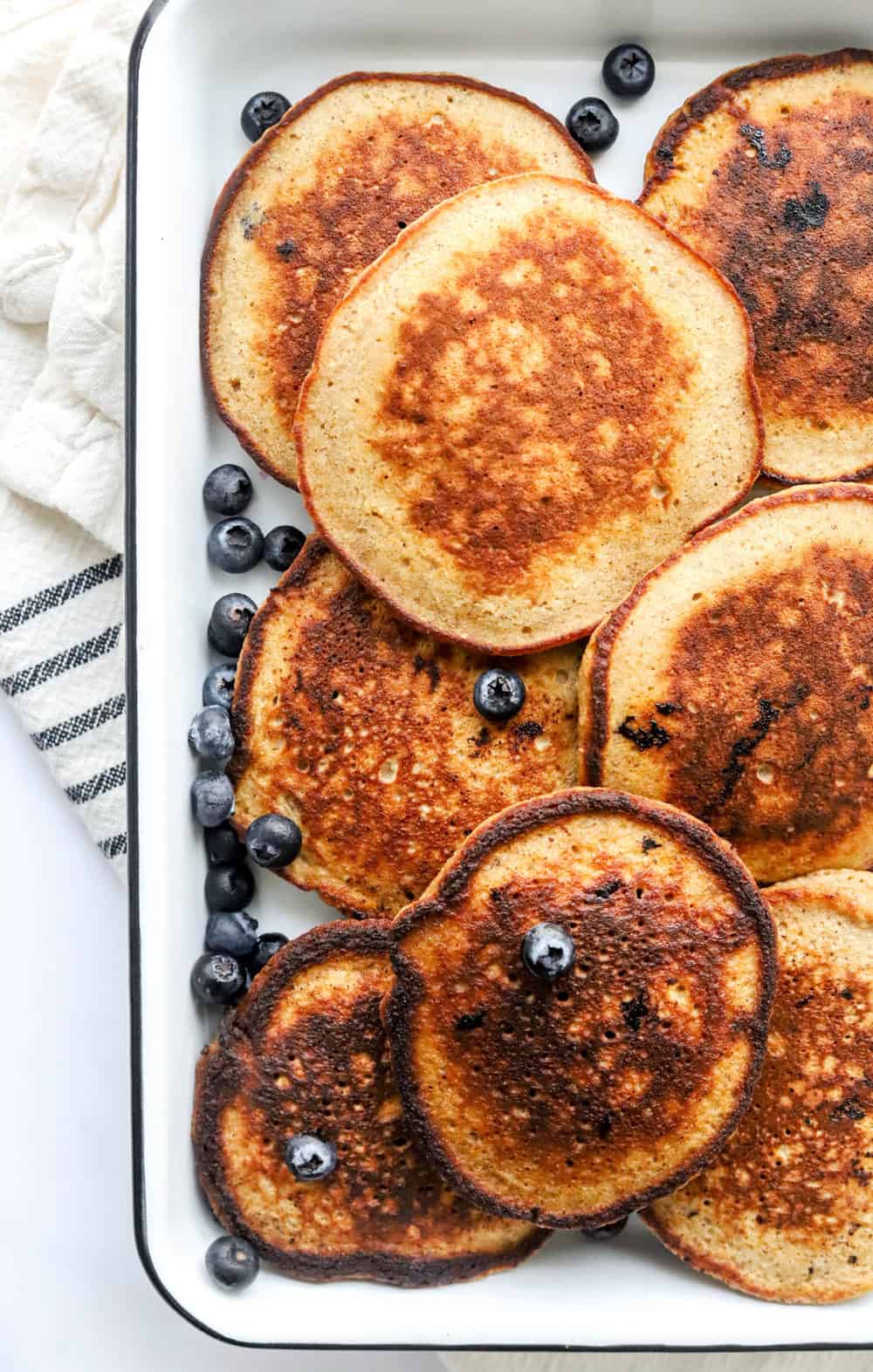 Healthy pancakes layered on a white tray with blueberries sprinkled around the tray. 