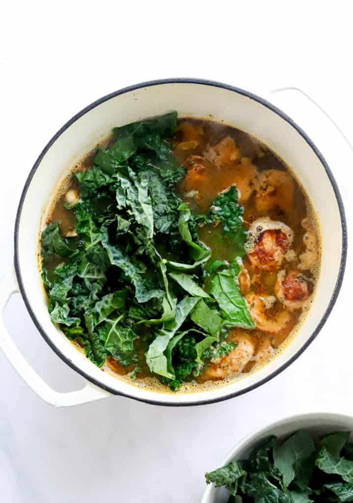 Soup pot filled with sausage soup with a pile of chopped kale on top.