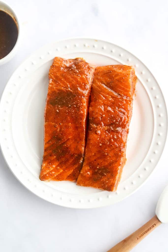 Raw seasoned salmon on a round white plate.