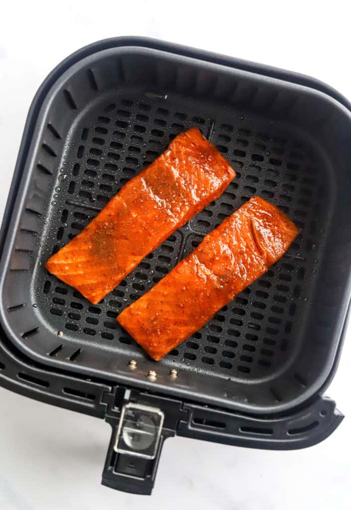 Cajun salmon uncooked in a black air fryer basket. 