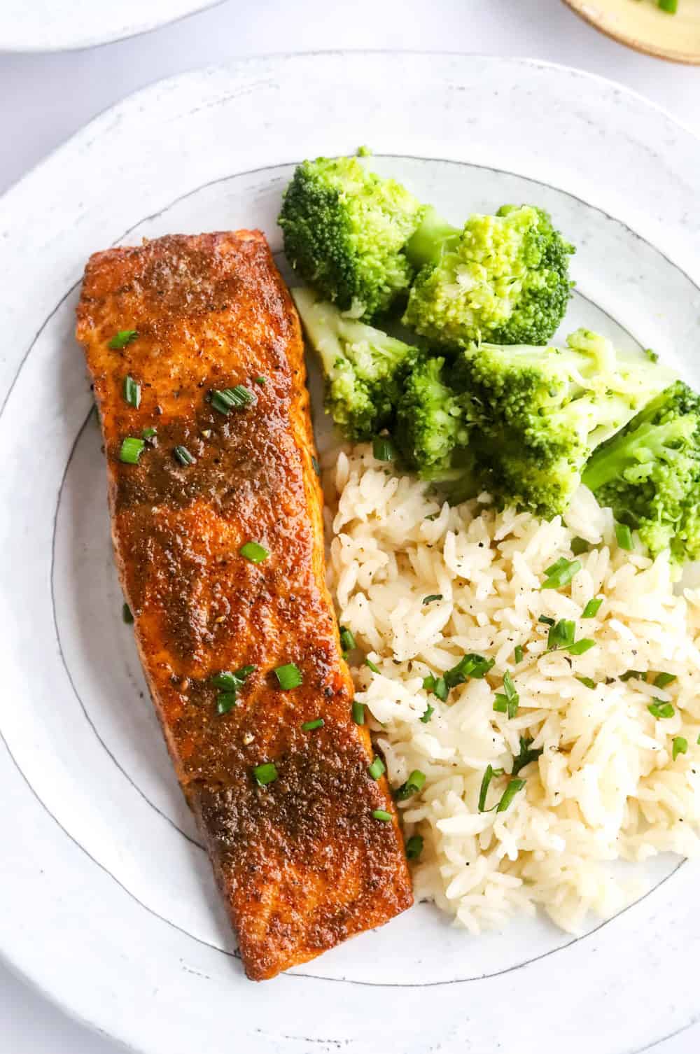 Close up of salmon with seasoning on it, on a plate with rice and broccoli. 
