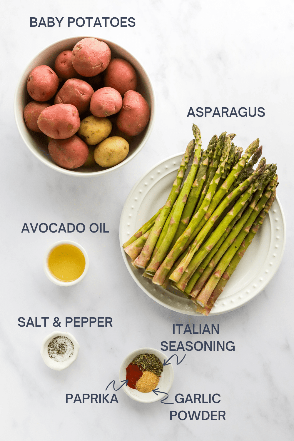 Bowl of red and gold potatoes with a bowl of asparagus, small bowl of oil, bowl of spices and a bowl of salt and pepper in front of it. 
