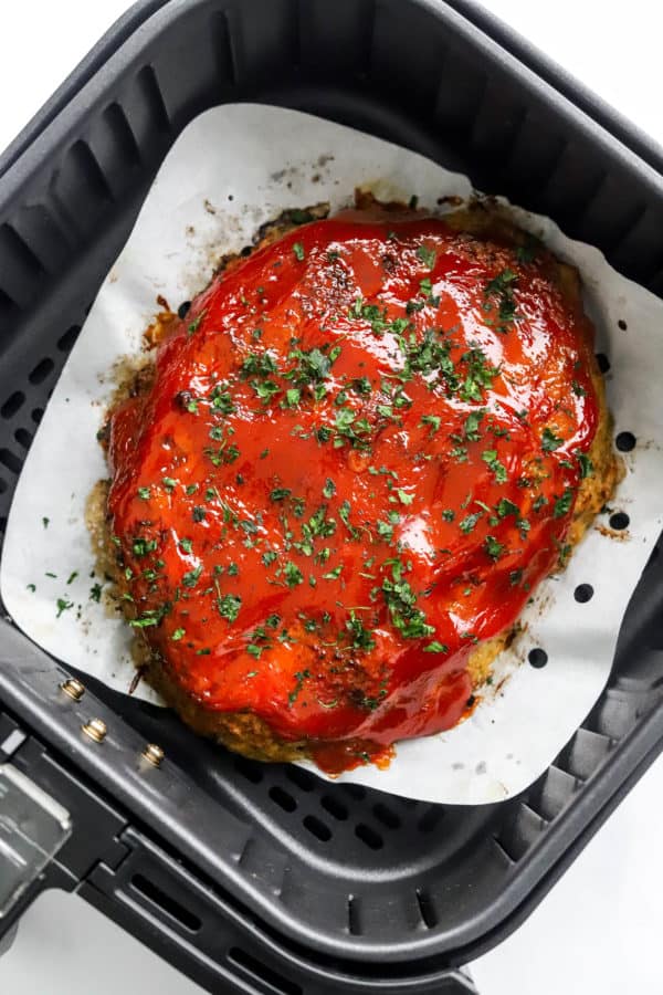Cooked meatloaf with red sauce and parsley on top in an air fryer.