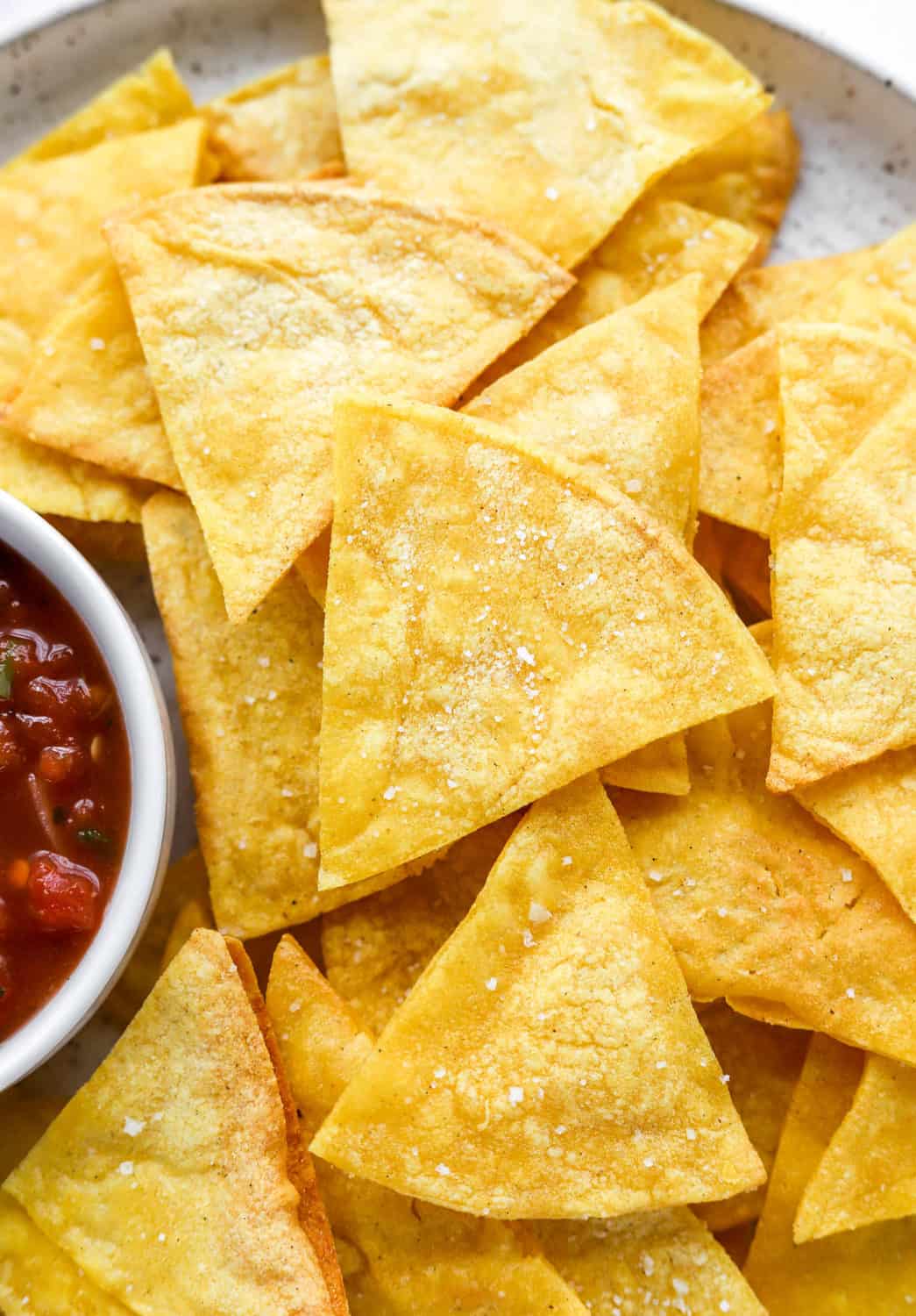 Pile of yellow tortilla chips with a dish of red salsa next to them. 