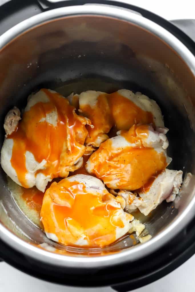 Chicken thighs covered in buffalo sauce in an instant pot. 