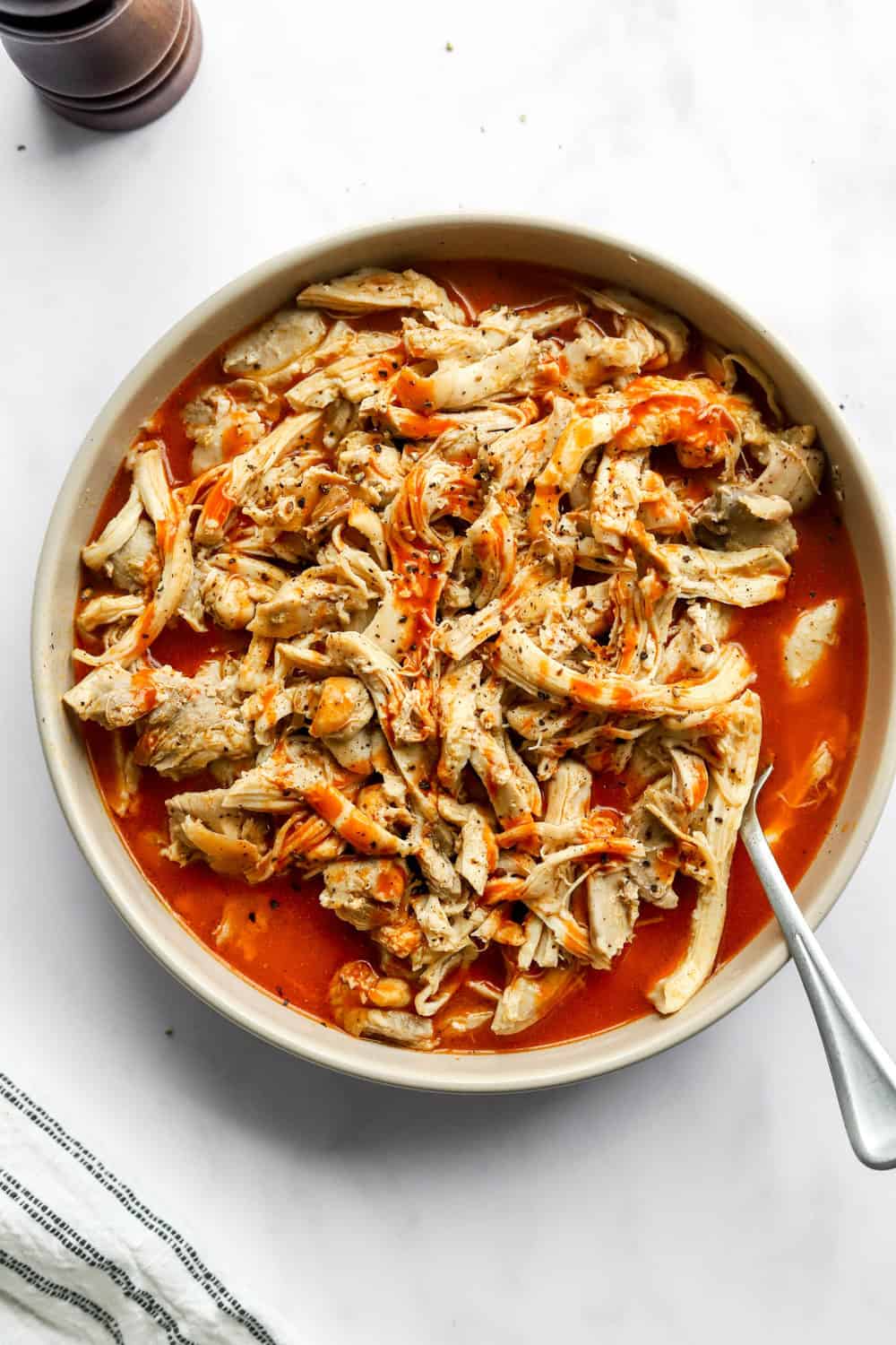 Shredded chicken covered in red buffalo sauce in a round dish with a fork in it. 