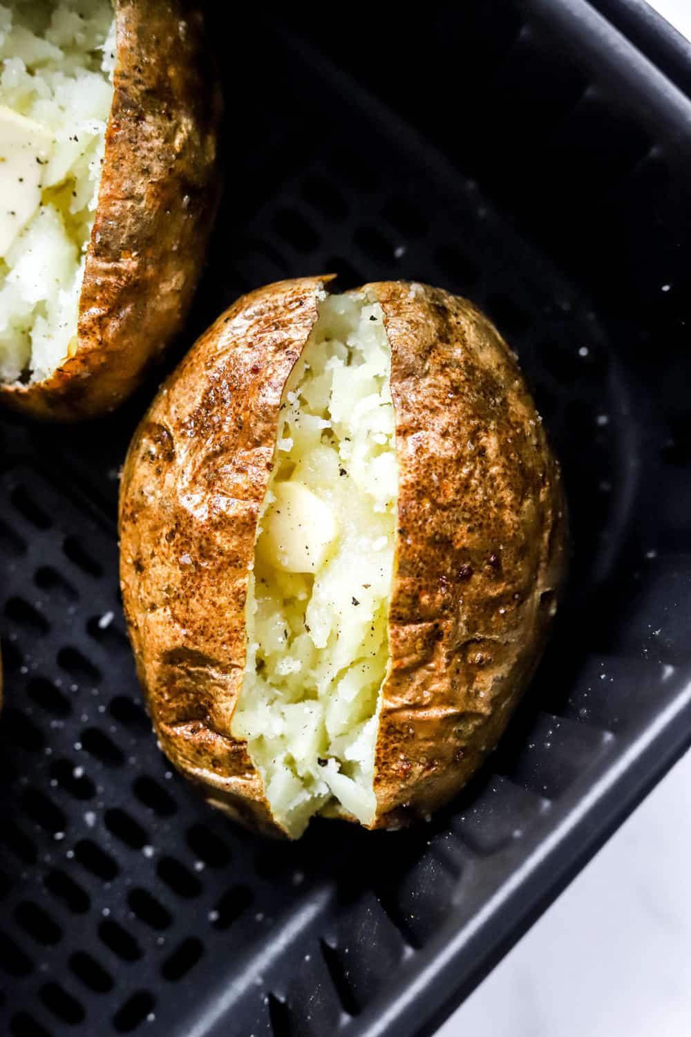 Cooked baked potatoes in a black air fryer basket. 