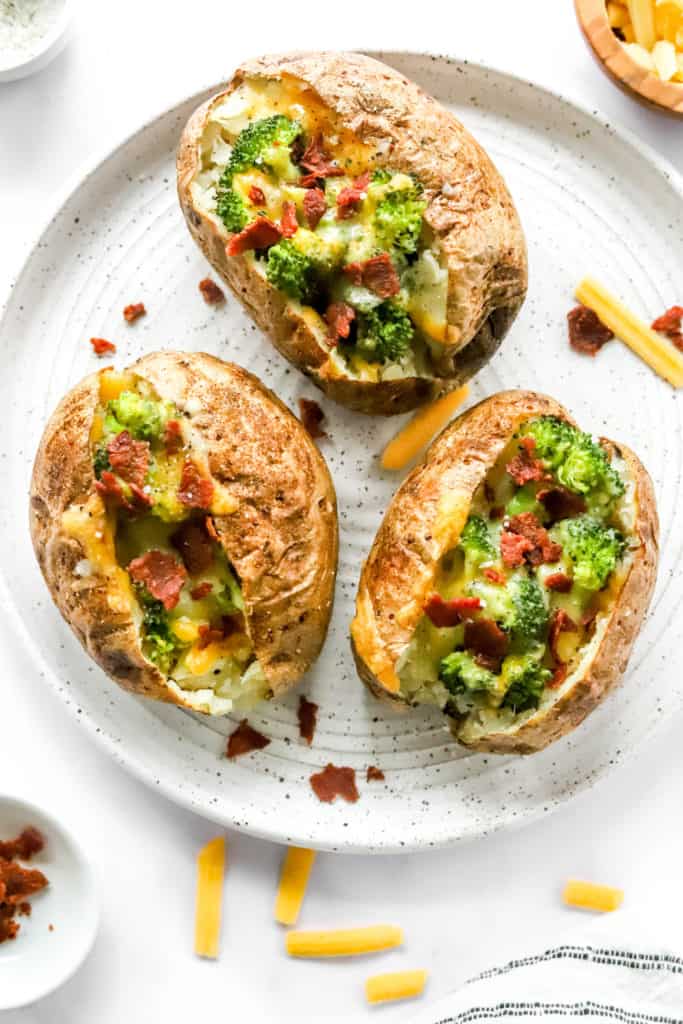 Broccoli, cheese and bacon loaded baked potatoes on a round white plate. 
