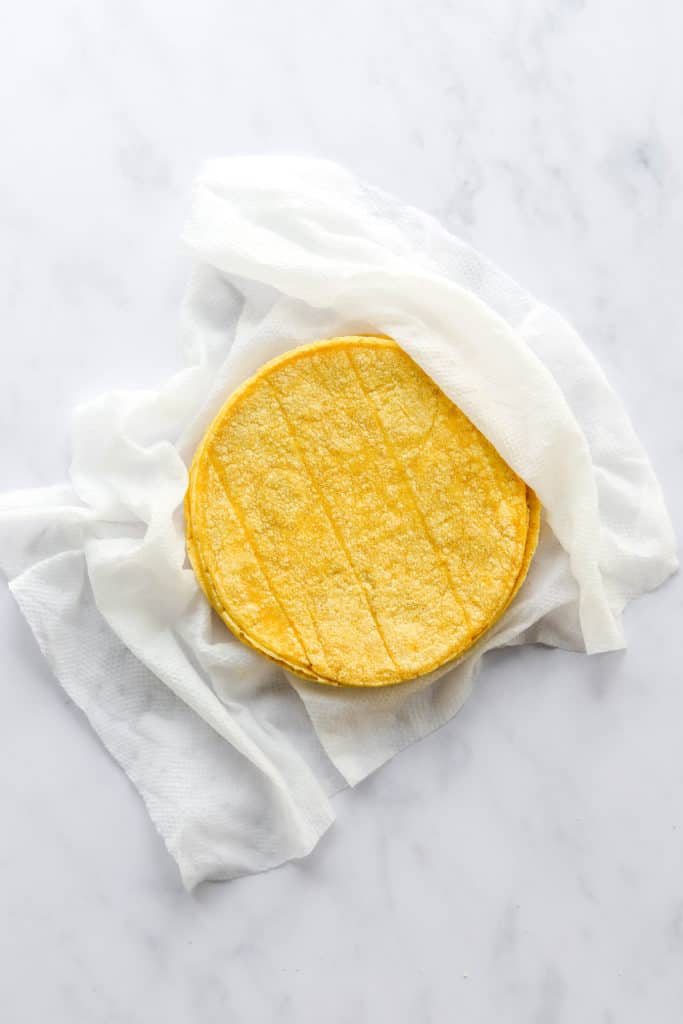 Yellow corn tortillas on top of a white, damp paper towel. 