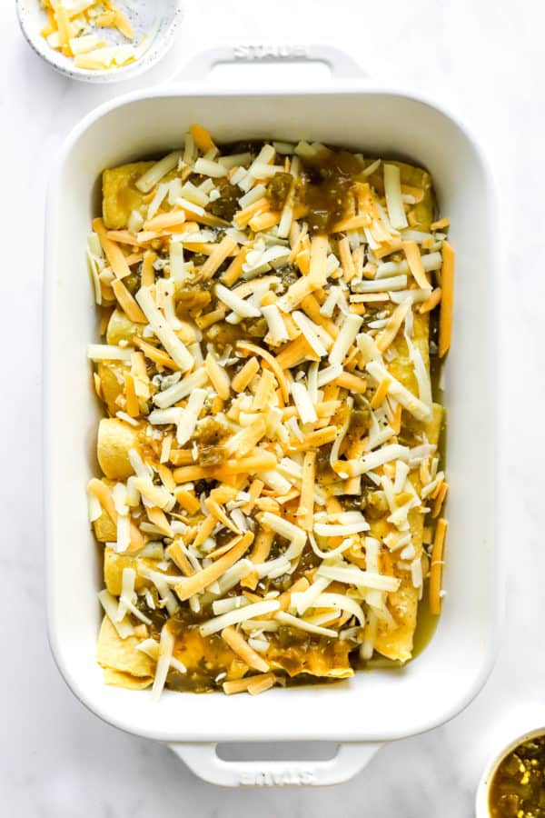 White baking dish filled with chicken enchiladas and topped with shredded cheese.