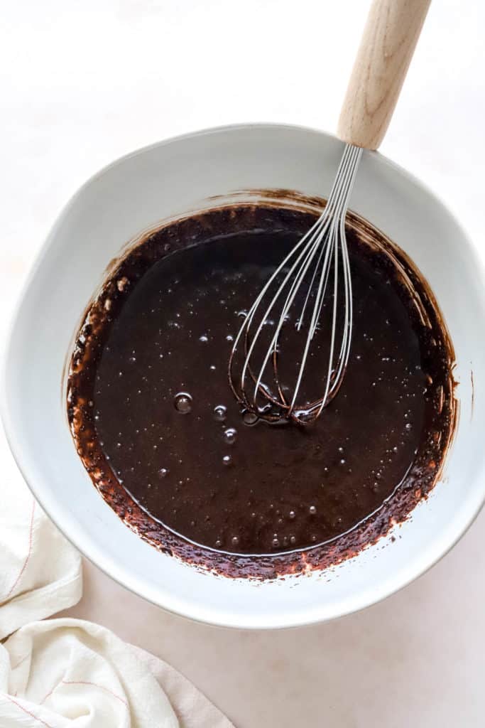 Dark chocolate cookie batter in a white bowl with a whisk. 