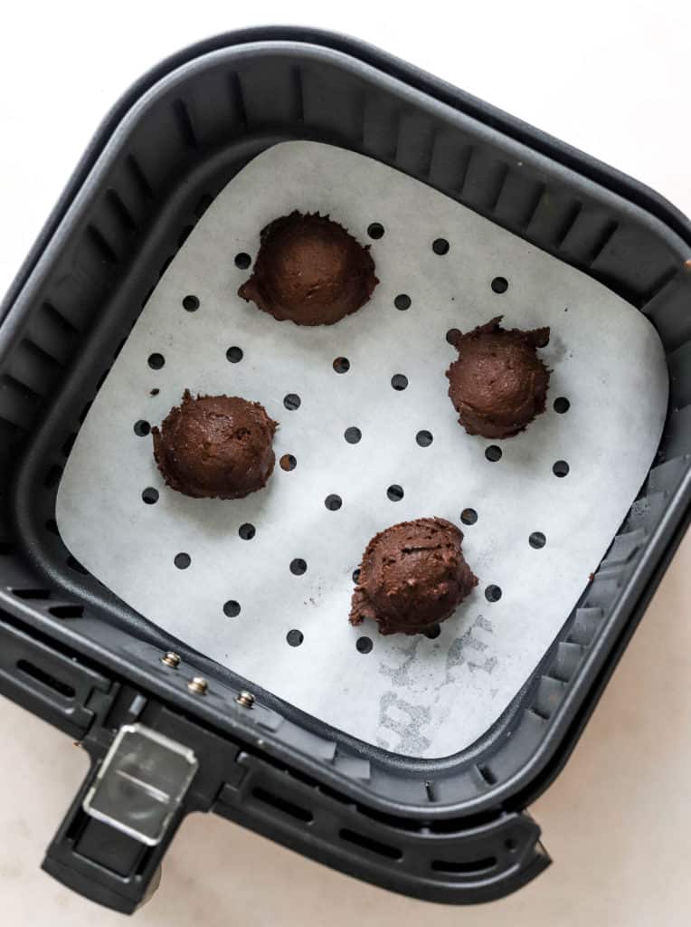 4 round balls of chocolate cookie dough in an air fryer basket. 