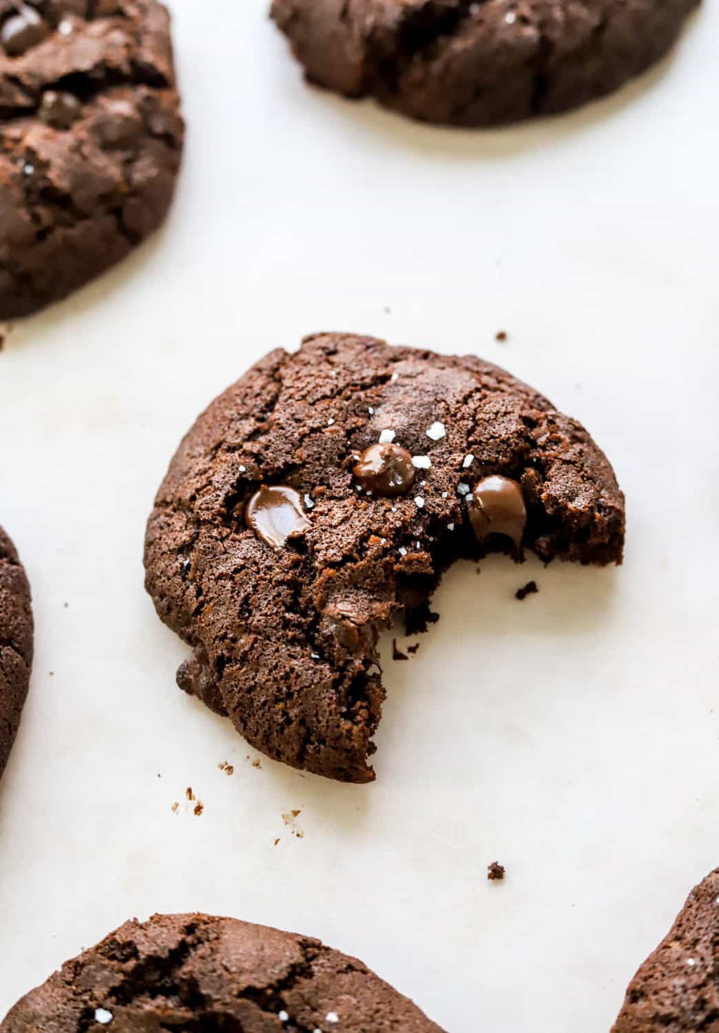 Dark chocolate cookie with melty chocolate chips in it with a bite taken out of it and more cookies around it. 