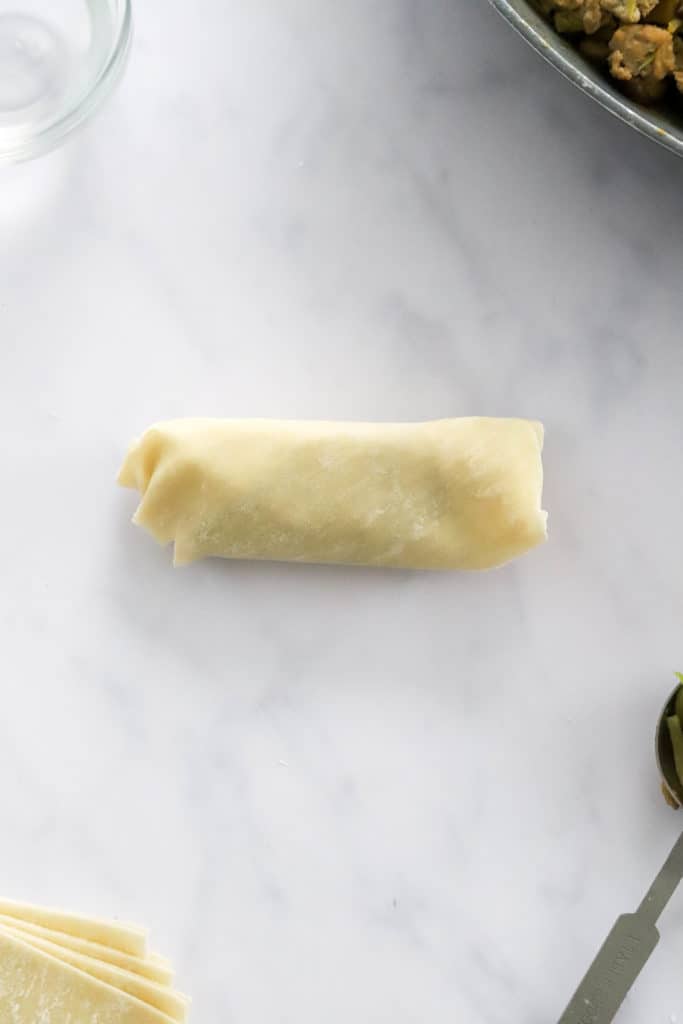 Uncooked rolled egg roll on a white surface. 
