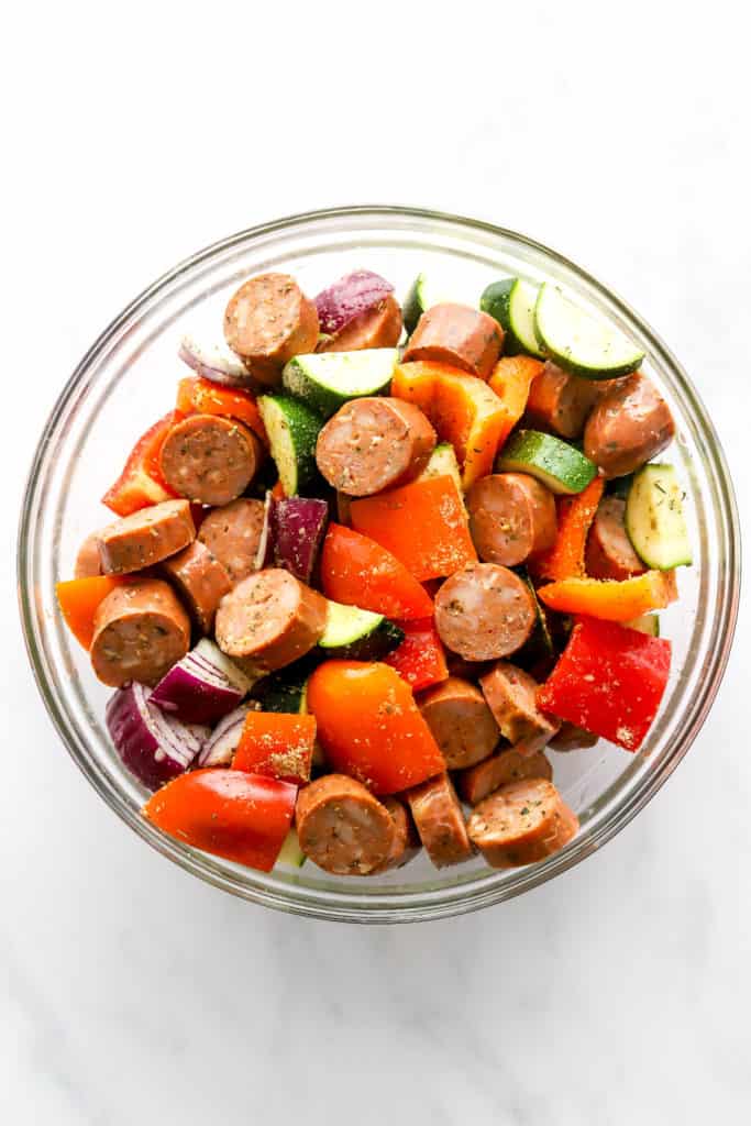 Chicken sausage cut into rounds in a bowl with chopped bell peppers, zucchini and red onion.