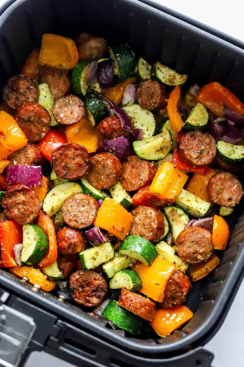 Sausage and veggies in a square, black air fryer basket. 