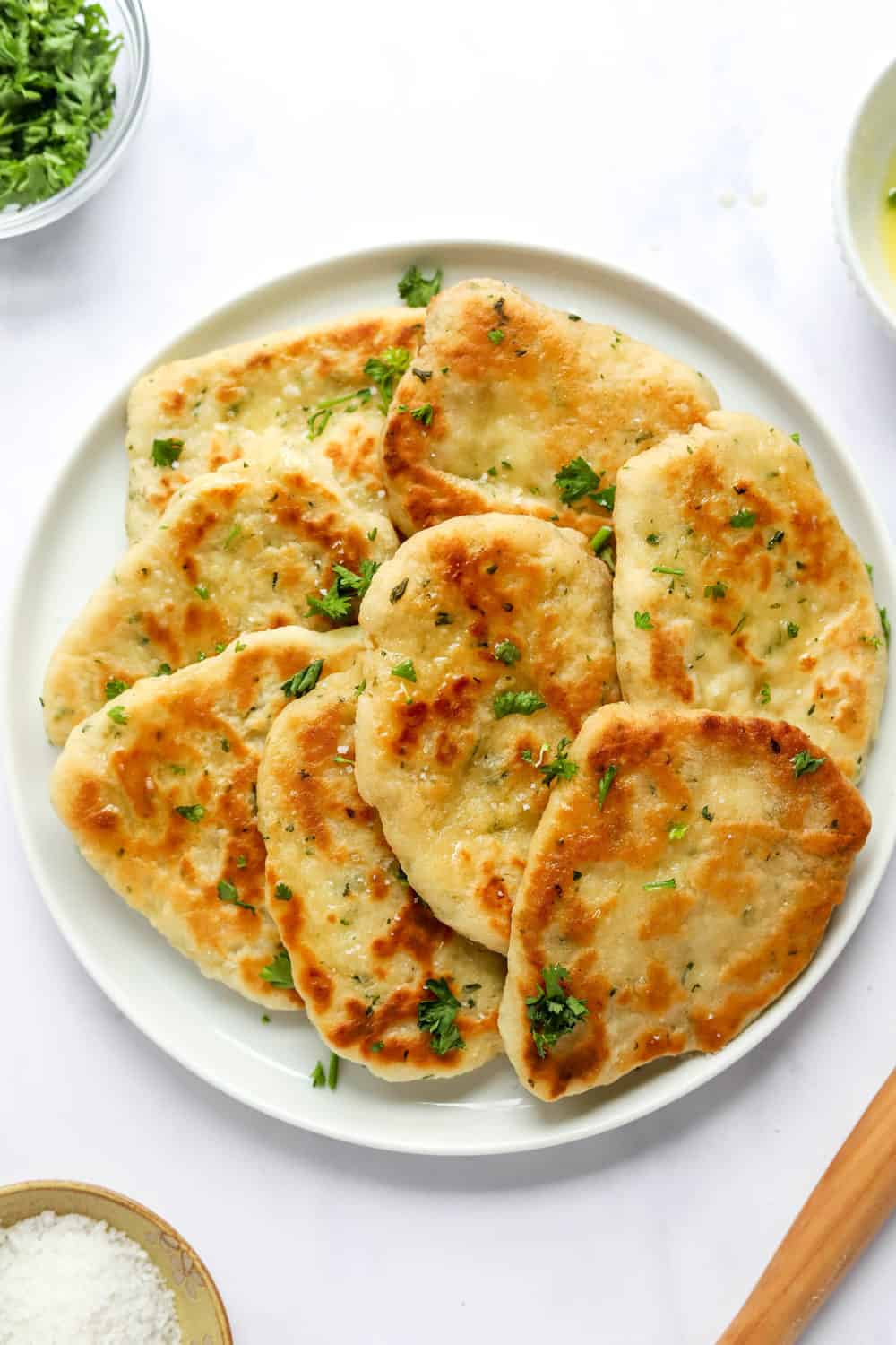 Plate full of naan bread with a bowl of parsley behind it. 