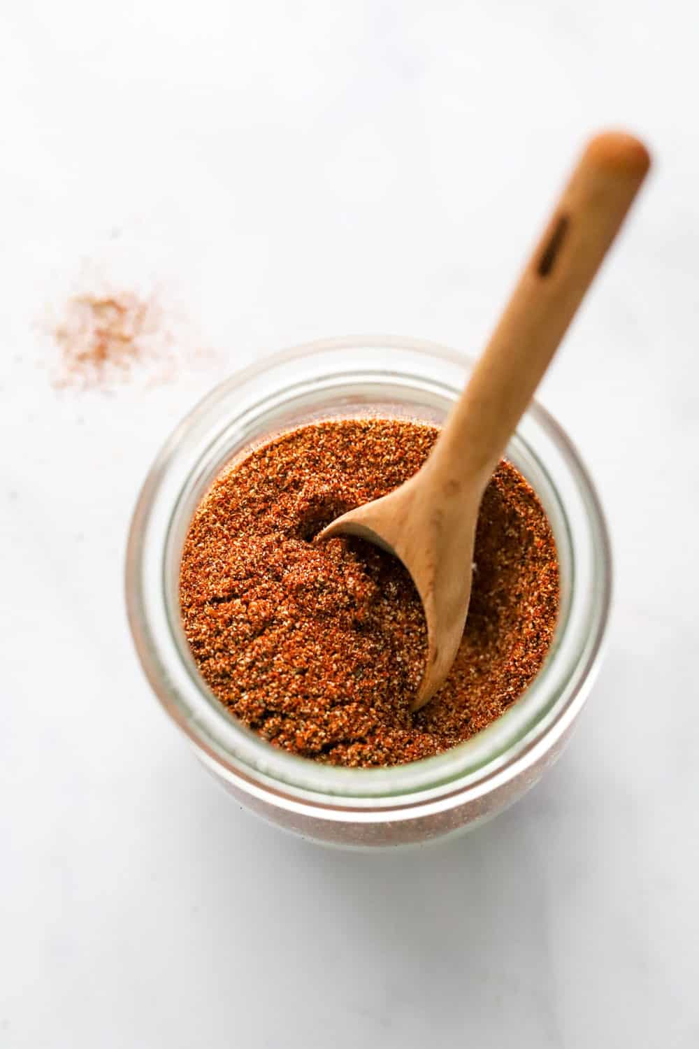 Gluten free taco seasoning in a glass jar with a small wooden spoon sticking to of the jar. 