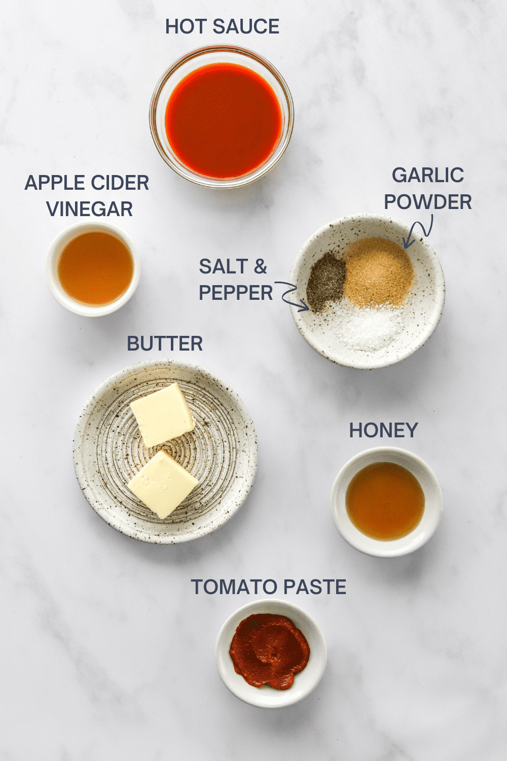 Buffalo sauce ingredients in bowls with labels over each ingredient on a white surface. 
