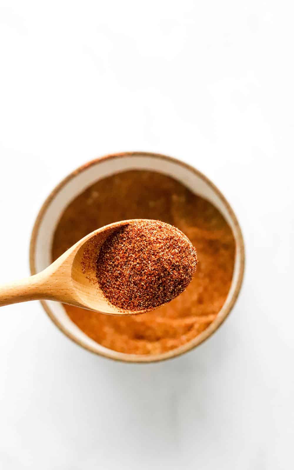 Close up of a wooden spoon with taco seasoning in it with a bowl of seasoning under it. 