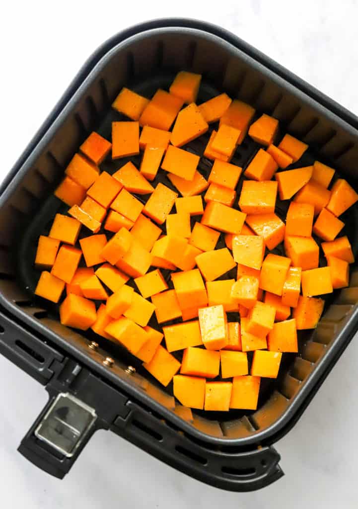 Cubes of yellow squash in a black air fryer basket. 
