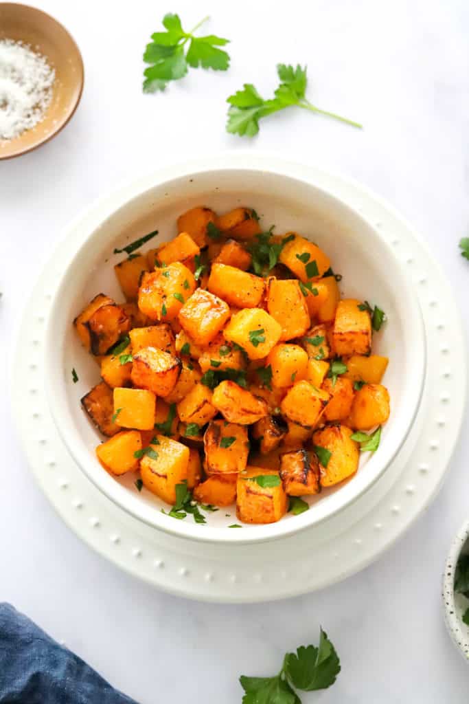 Roasted cubes of squash in a white serving bowl with chopped parsley on it. 