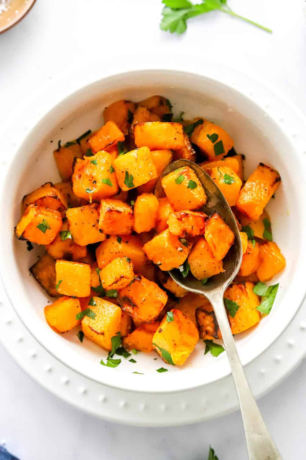 Cubed, cooked air fryer butternut squash in a round, white bowl with a spoon in the bowl with cubes of squash on it. 