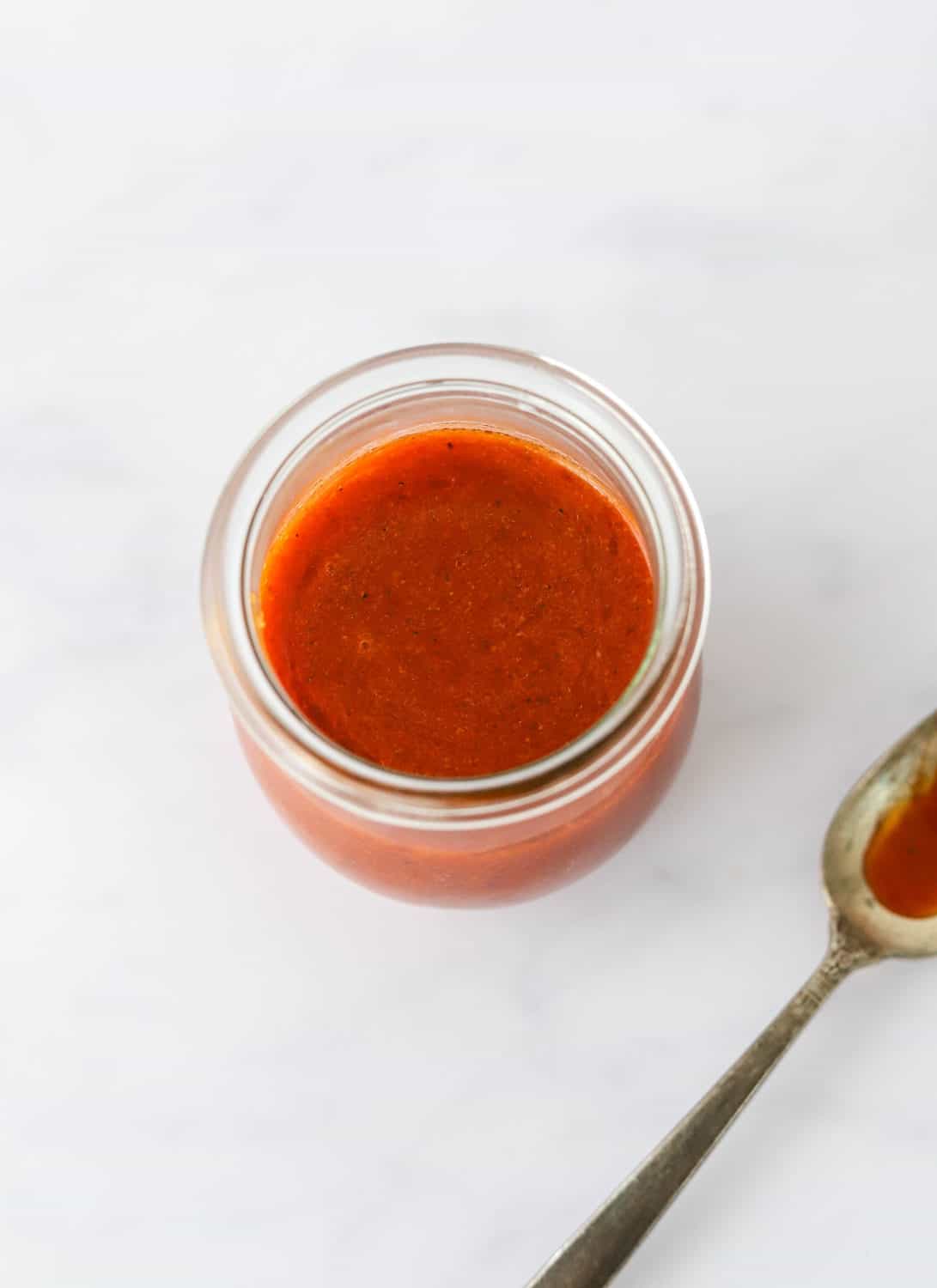 Round, glass jar filled with buffalo sauce with spoon next to it with some sauce on the spoon. 