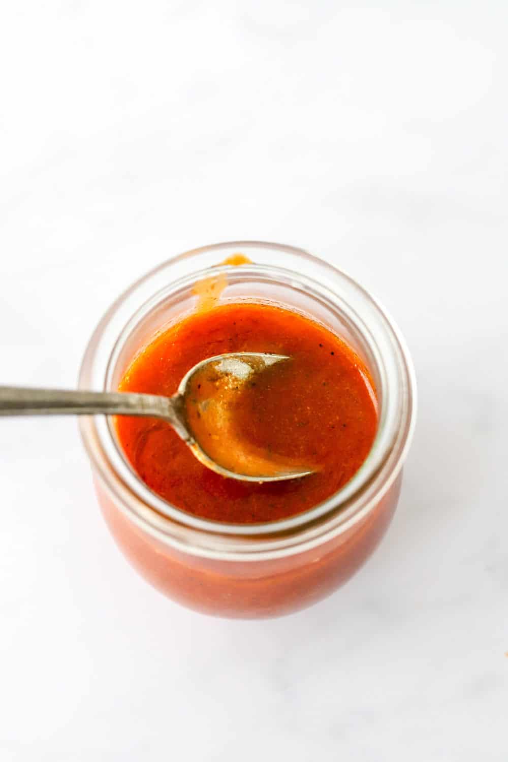 Spoon in a glass jar filled with red buffalo sauce. 