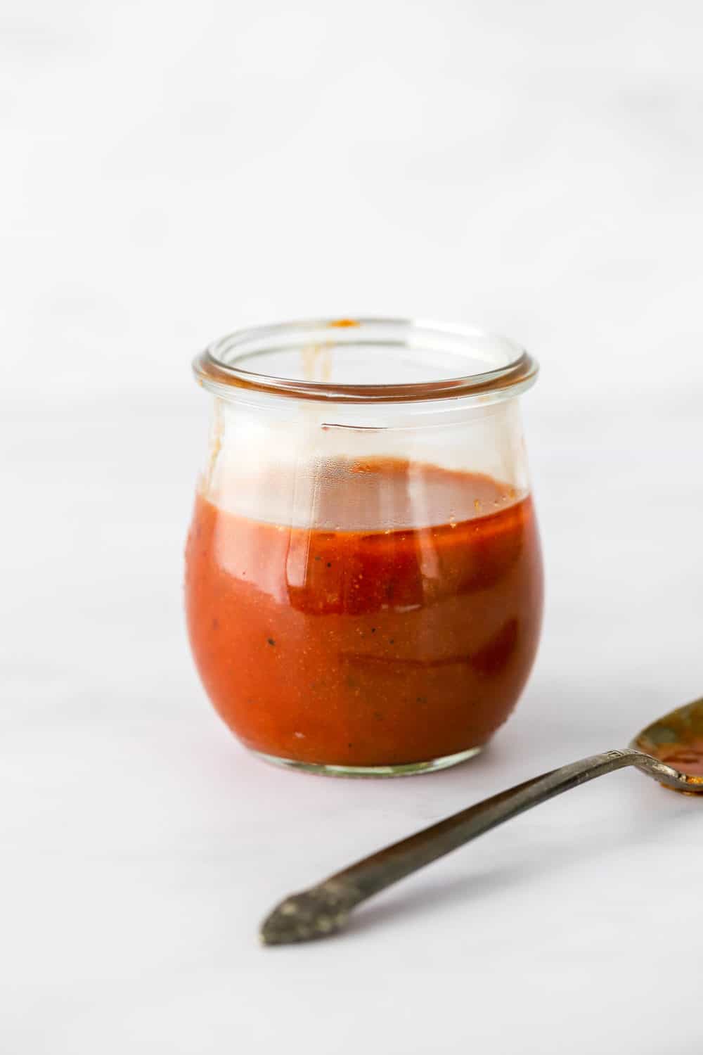 Small glass jar filled with healthy buffalo sauce with a silver spoon next to the jar. 