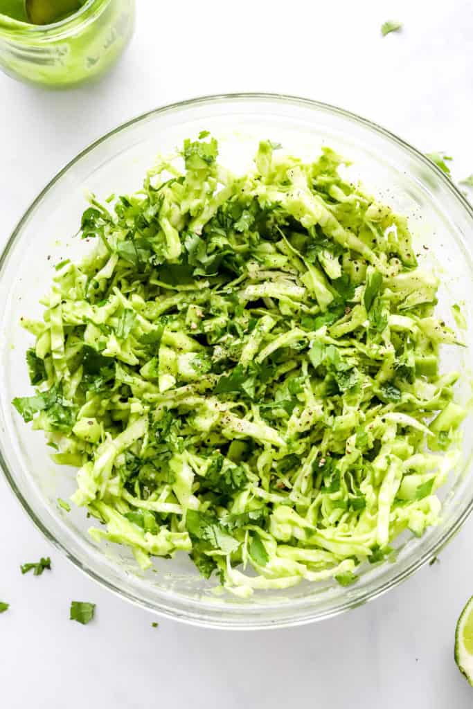 Green cabbage slaw mixed with a creamy dressing in a round, glass bowl. 