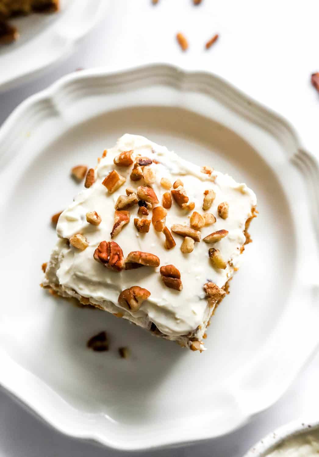 Square slice of carrot cake with frosting and chopped pecans on top of it. 