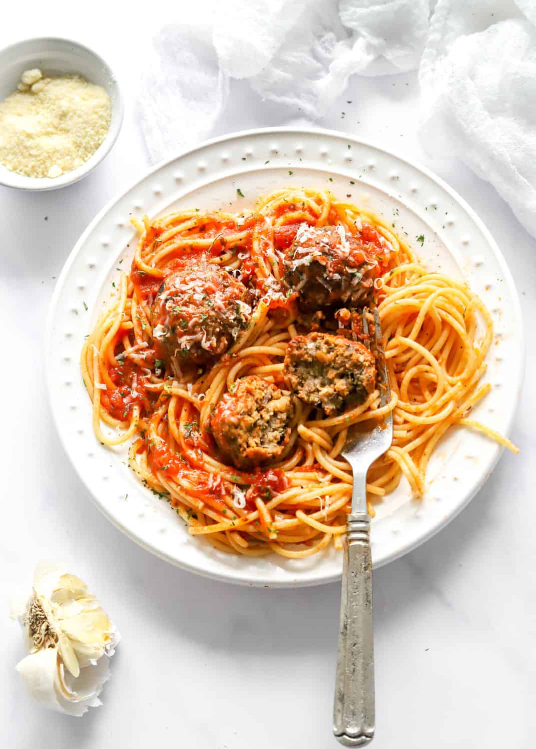 Meatless meatballs on a plate over cooked spaghetti covered in tomato sauce. With on of the meatballs sliced open. 